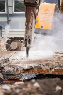 Close-up of an excavator breaking up concrete surrounded by dust and rubble, demolition site,