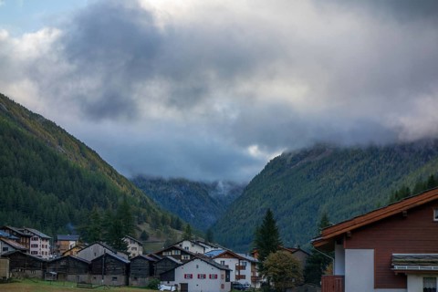 Village in the valley of the Alps with houses surrounded by cloudy mountains under an autumn sky,