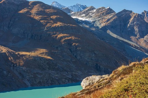 A mountain lake under bright sunlight, surrounded by autumn-coloured mountains and snow-capped