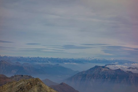 A vast mountain landscape with visible peaks and distant mountain ranges under a cloudy sky, Saas