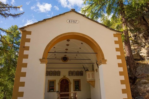 Historic church from 1747 in white colour, surrounded by forest and mountains under a clear sky,