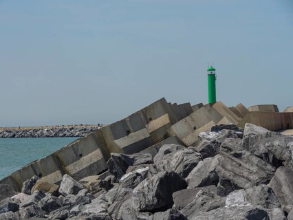 Stable rock formations and a green lighthouse at the breakwater along the coast under a clear sky,
