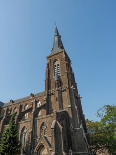 Large Gothic church with high tower and pointed arch windows made of red brick under a clear sky,