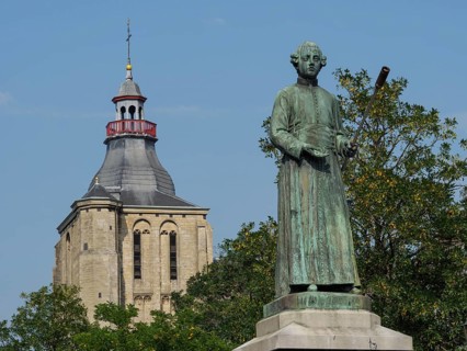 Bronze statue in front of a church building and green trees under a blue sky, historical monument,