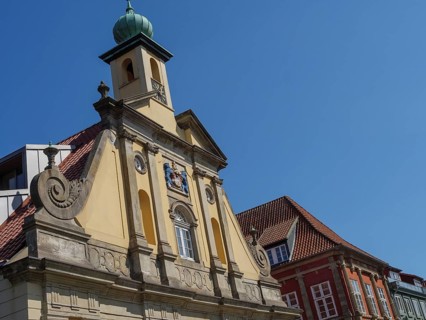 Baroque building in the old town centre with a pale church tower in the background under a blue