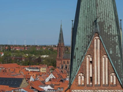Church towers and roofs of a town, surrounded by landscape and wind turbines in the background,