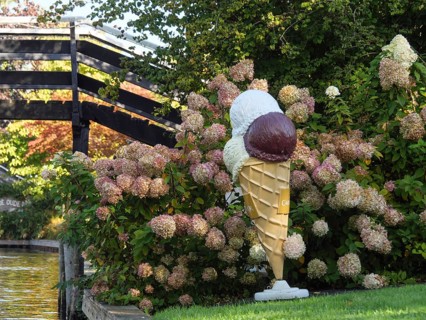 Large ice-cream cone decoration between hydrangea flowers on a canal next to a wooden bridge,