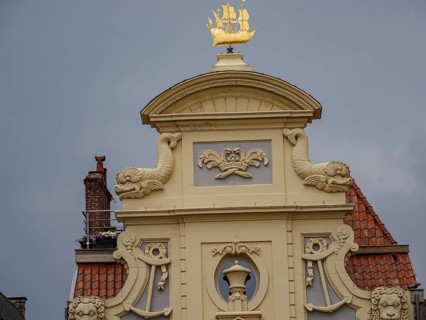 Detailed view of a building gable with golden decorations and a coat of arms. Grey cloudy sky,