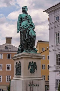 Monument to Mozart on a square surrounded by historic buildings under a cloudy sky, Salzburg,
