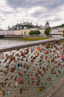 Love locks on a bridge railing with a view of historic buildings along a river, Salzburg, Austria,