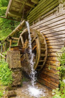 Rustic wooden watermill, water flows over the large mill wheel in the forest, Gosau, Austria,