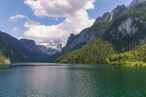 An unspoilt mountain lake, framed by high peaks and dense forests under a cloudy sky, Gosau,