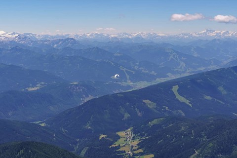 Aerial view of a mountainous landscape with a paraglider in the foreground under a clear sky,