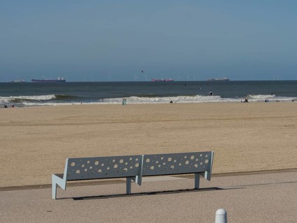 Bench with holes on the beach, in the background the sea and a slightly cloudy sky, scheveningen,