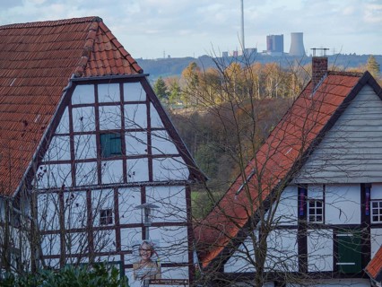 View of half-timbered houses with red roofs and chimneys in a wide landscape with a cloudy sky,