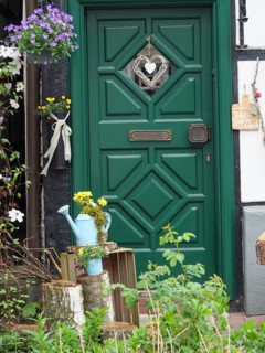 Rustic green door of a half-timbered house, decorated with flowers and a watering can in a