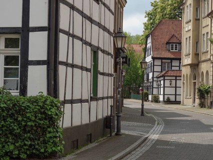Historic half-timbered houses on a quiet, cobbled street with street lamps and green shutters,