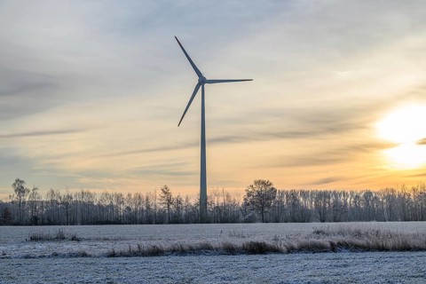 A large wind turbine stands on a snow-covered field at sunset, surrounded by bare trees, Velen,