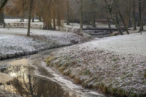 A small stream meanders through a wintry park landscape covered in snow and frost, Velen, North