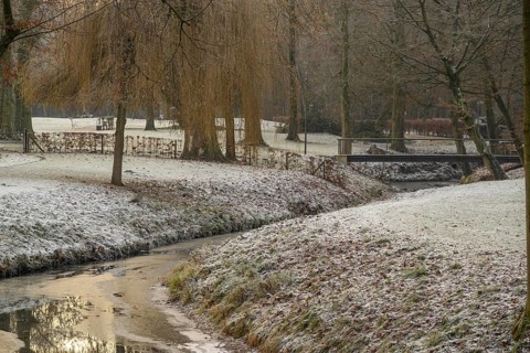 Frost-covered trees and grass surround a small river with a bridge in a wintry park, Velen, North