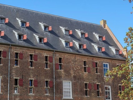 Historic building with many sloping skylights and red shutters under a clear sky, Doesburg,