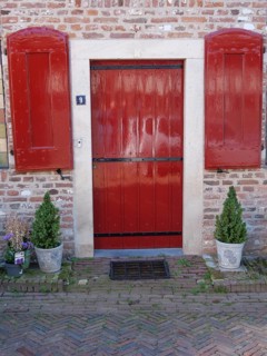 Red door with shutters surrounded by brick wall and potted plants, Doesburg, Netherlands