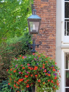 Close-up of a street lamp with a flowering hanging basket in front of a brick building with
