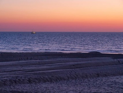 A boat sails on the sea during sunset, the beach shows traces in the sand and the atmosphere is