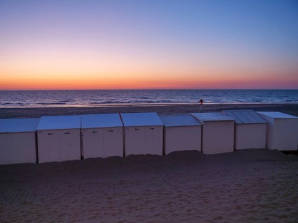 White beach huts at dusk, with an intensely coloured sunset and calm sea, de haan, Belgium, Europe