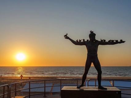 A sculpture on the beach at sunset, the sea in the background. The atmosphere is calm and