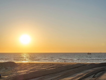 The sun sets over the sea, a boat can be seen in the distance, the atmosphere is calm and peaceful,
