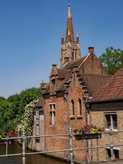 Picturesque scene with a canal, flowers and a bridge against the backdrop of a church tower,