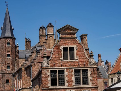 Detailed facades of historic buildings with many bricks and towers under a bright blue sky, Bruges,