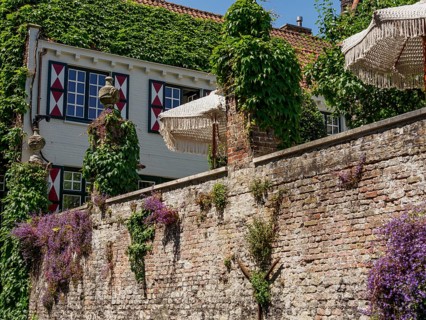 An ivy-covered house with decorative shutters, umbrellas on a stone wall, lined with red tiled