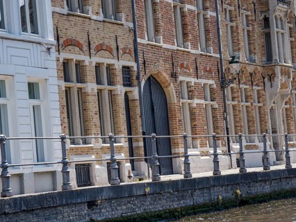 Detailed historic brick faÃ§ade with large windows and a wrought-iron railing on the canal, Bruges,