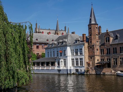 Gothic buildings and church towers reflect in the water under a clear blue sky, Bruges, Belgium,