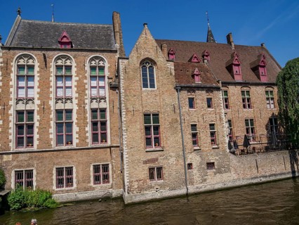 Historic buildings with brick facades along a canal under a bright blue sky, Bruges, Belgium,