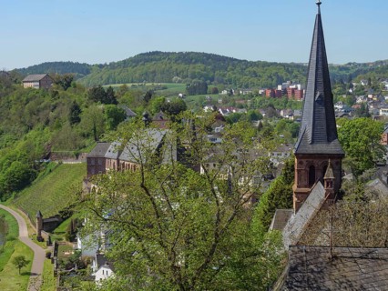 A view over a town with a striking church spire, surrounded by green hills and trees, Saarburg,