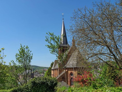 A church tower rises above a tree- and plant-covered environment under a clear sky, Saarburg,