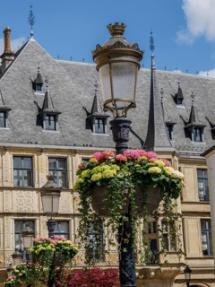 Hanging flower arrangements around an antique street lamp, behind it a historic building with