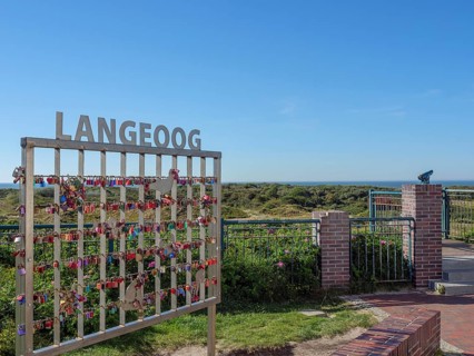 A fence with love locks in front of a vast natural backdrop under a blue sky on Langeoog, langeoog,