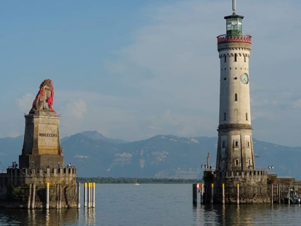 Lighthouse and lion statue at the entrance of a harbour, mountain landscape in the background,