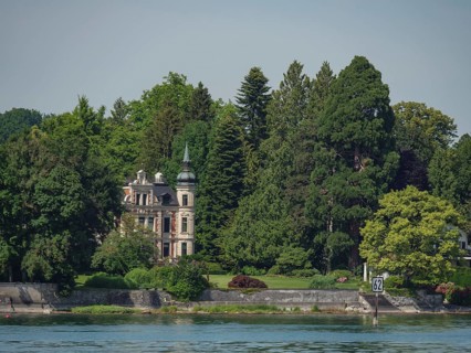 Elegant castle with characteristic towers and facades, surrounded by dense forest and water on the