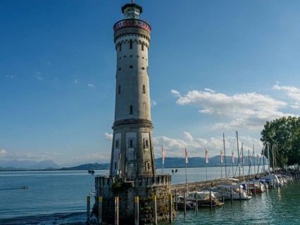 Lighthouse next to boats on the lakeshore with clear sky and summer atmosphere, Lindau, Bavaria,