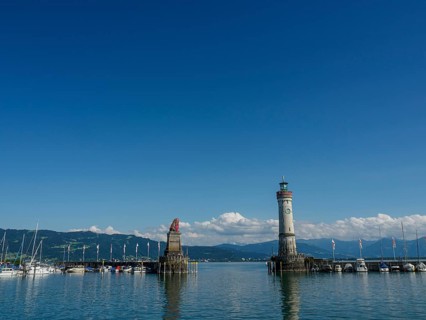 A lighthouse and a statue flanked by boats in the harbour on a clear day, Lindau, Bavaria, Germany,