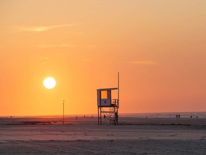 A rescue tower stands on the beach, the sky is coloured orange by a breathtaking sunset, juist,