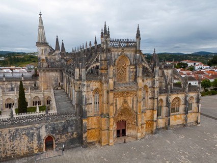 Impressive Gothic cathedral with a grand entrance and detailed towers under a cloudy sky, aerial