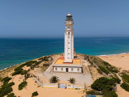 White lighthouse on the coast with a view of the sea and the beach under a clear sky, aerial view,