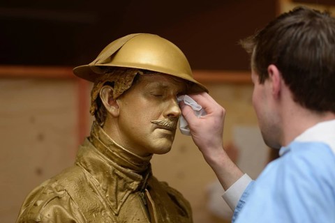 A make-up artist applies gold paint to an actor's face before a performance