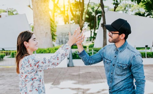 Girl and a guy shaking hands on the street. Two young smiling friends greeting in the street.
